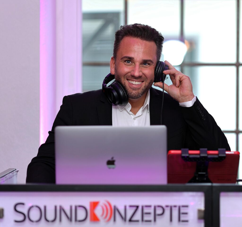 DJ hinter DJ-Booth bei einer Hochzeit mit Hopfhörer in der Hand